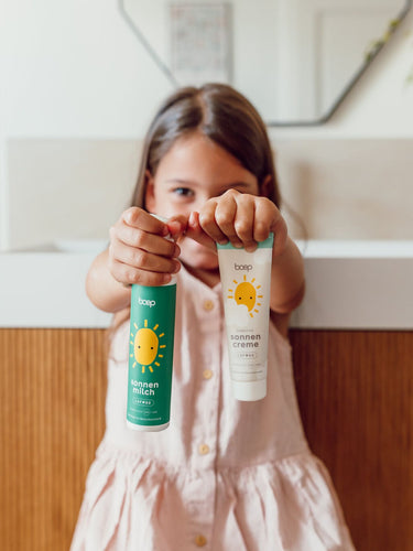 Mädchen hält die mineralische Sonnenmilch und die mineralische Sonnencreme Sensitiv von das boep für Schwangere, Babys und empfindliche in die Kamera.