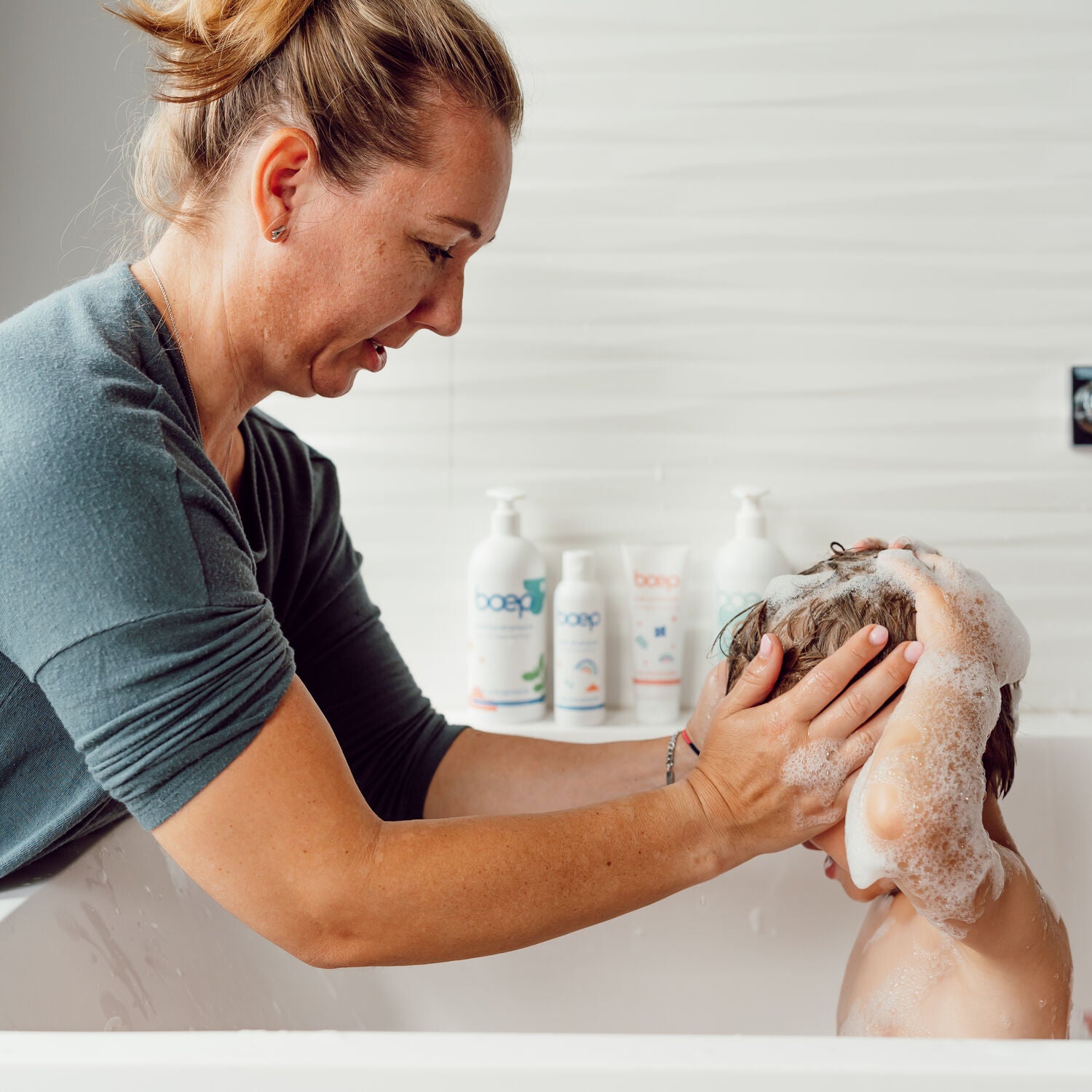 Mutter schäumt Kind mit Shampoo die Haare ein im Hintergrund stehen verschiedene Pflegeprodukte von das boep