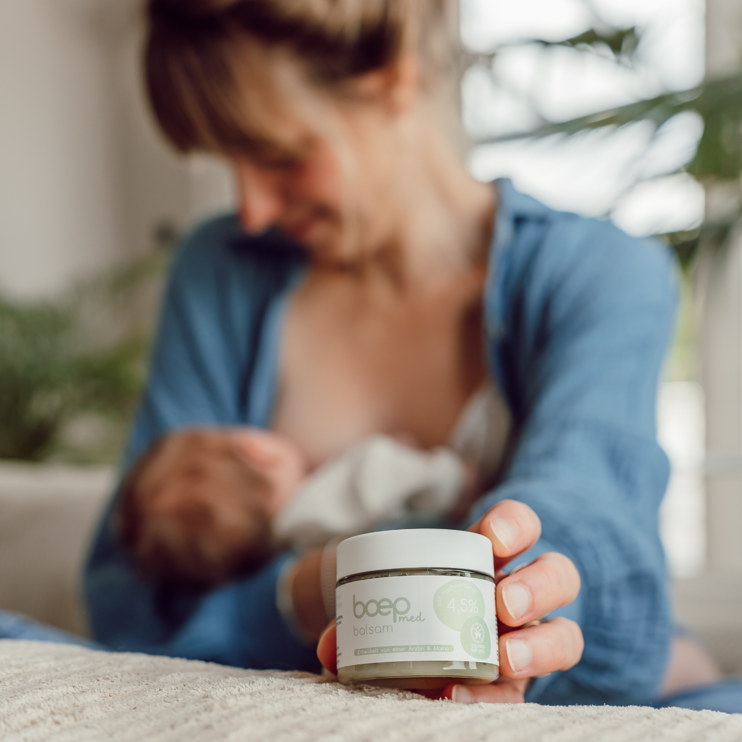 Stillende Frau mit Baby im Arm hält das Naturkosmetik med Balsam für sehr empfindliche Haut und Neurodermitis von das boep in die Kamera