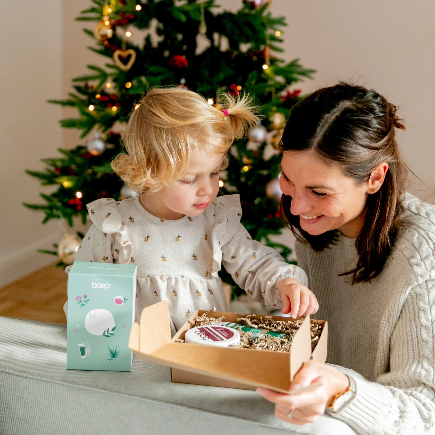 Mama und Tochter packen ein Geschenkset von das boep vor dem Weihnachtsbaum aus