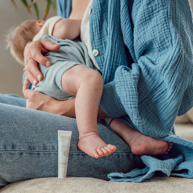 stillende Mama mit Baby und med Balsam Mini  als veganes Brustwarzenbalsam im Vordergrund