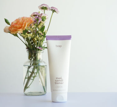 Das boep med Conditioner für empfindliche Kopfhaut ohne Duftstoffe steht auf dem Tisch und im Hintergrund ist eine Blumenvase zu sehen.