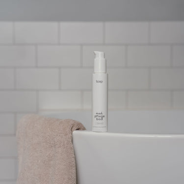 Naturkosmetik med Pflegebad von das boep und annisbuntewelt pflegender Badezusatz für Babys, sehr empfindliche Haut und Neurodermitis steht auf einem Badewannenrand mit einem Handtuch daneben
