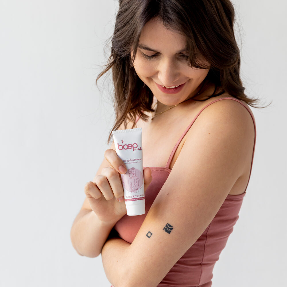 Junge Frau mit Tattoos am Arm hält Naturkosmetik Tattoopflegecreme von das boep für die Tattoopflege in der Hand