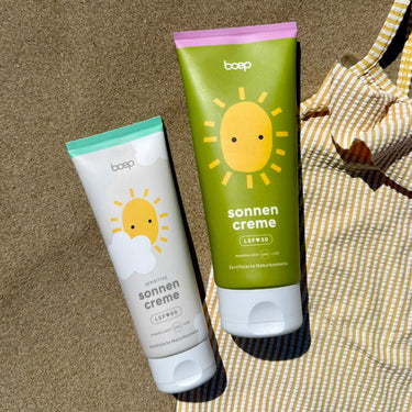 Mineralische Sonnencreme mit LSF30 und mineralische Sonnencreme Sensitiv mit LSF50 von das boep liegen im Sand mit einem Badeanzug daneben