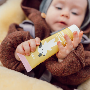Baby hält den Naturkosmetik Wind und Wetterbalsam von das boep für Babys und Kinder gegen trockene Babyhaut als Kälteschutz in der Hand.
